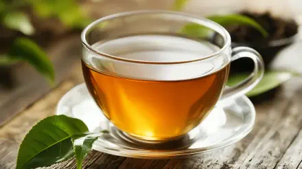 A clear glass cup filled with vibrant oolong tea sits on a saucer, surrounded by fresh tea leaves, set against a rustic wooden background. 4K Ultra HD wallpaper.
