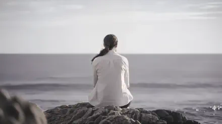 A person sits on a rock, gazing out at a calm ocean under a serene sky, embodying an 'empty inside' feeling. A stunning 4K Ultra HD desktop wallpaper.