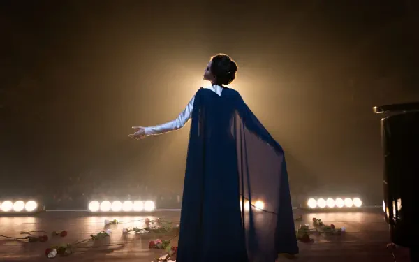 A stunning 4K Ultra HD wallpaper from the movie Maria (2024), featuring a performer in a flowing cape, standing in spotlight with rose petals scattered on stage.