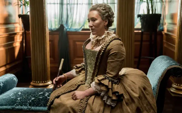 A character from the TV show Outlander, seated in a grand setting, wearing an elaborate vintage dress and poised with a quill, captured in rich detail for a 4K Ultra HD background.