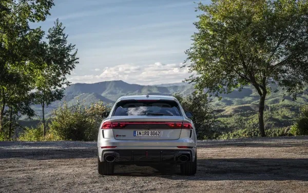 A rear view of an Audi RS Q8 parked in a scenic landscape, surrounded by lush greenery and mountains under a clear sky. A stunning 4K Ultra HD background for any desktop.