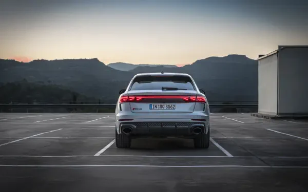 A sleek Audi RS Q8 parked in an empty lot, showcasing its modern design against a backdrop of mountains at sunset. A stunning 4K Ultra HD desktop wallpaper.