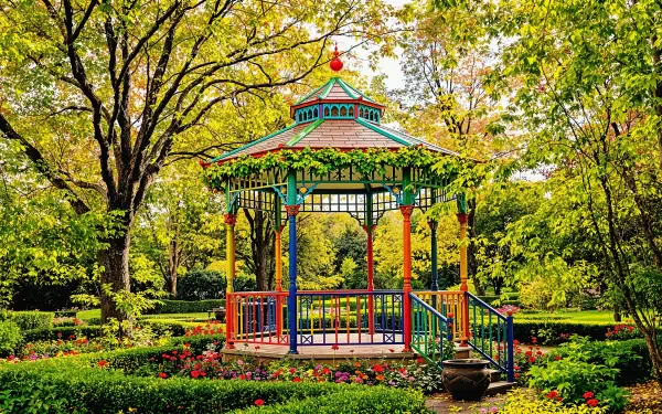 Colorful gazebo stands in a vibrant garden surrounded by lush greenery and blooming flowers, captured in a detailed 4K Ultra HD nature and architecture wallpaper.