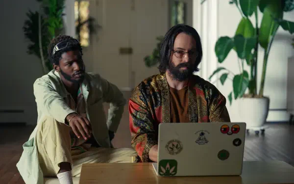 Two men are seated indoors, one working on a laptop while the other observes. The scene captures a moment from the TV show Tulsa King. 4K Ultra HD desktop wallpaper.