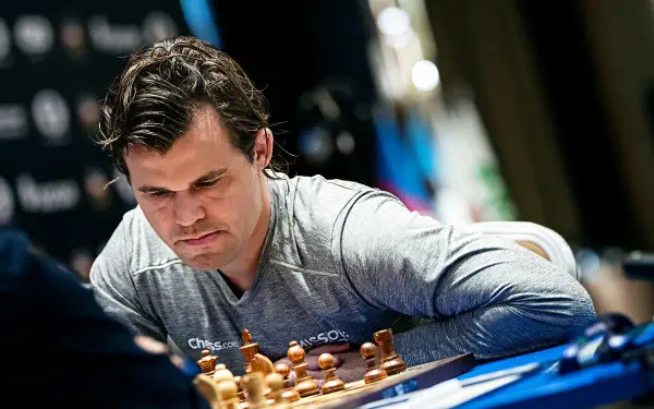 Magnus Carlsen intensely focuses on a chess game, surrounded by pieces and a competition backdrop, making this image a striking HD desktop wallpaper for sports and chess enthusiasts.
