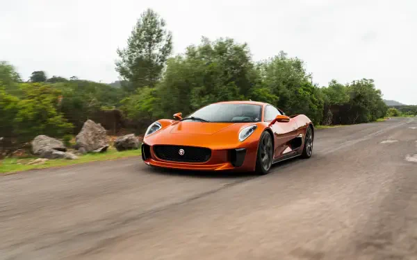 An orange Jaguar C-X75 sports car drives along a winding road, surrounded by lush greenery. This high-definition image serves as a striking desktop wallpaper and background.
