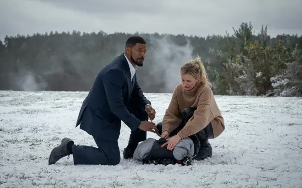 Cameron Diaz and Jamie Foxx in a tense scene from the movie Back in Action, kneeling in the snow as they assist a figure on the ground, framed by a dramatic winter landscape.