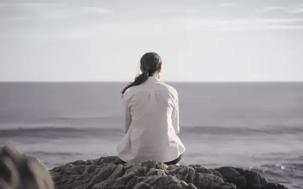 A person sits on a rock, gazing out at a calm ocean under a serene sky, embodying an 'empty inside' feeling. A stunning 4K Ultra HD desktop wallpaper.