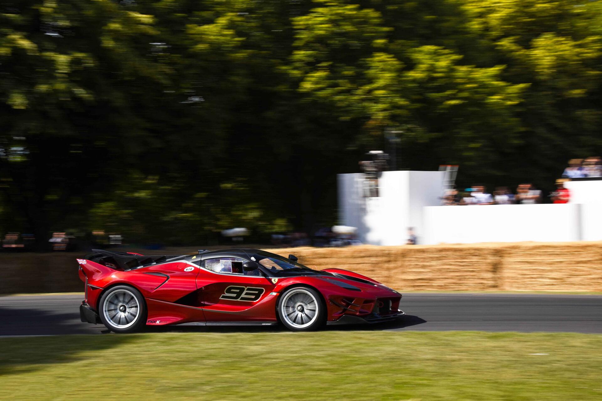 Red Ferrari race car (#93) streaks along a sunlit track with blurred trees and a haybale barrier — 5K Ultra HD PC desktop wallpaper and background.