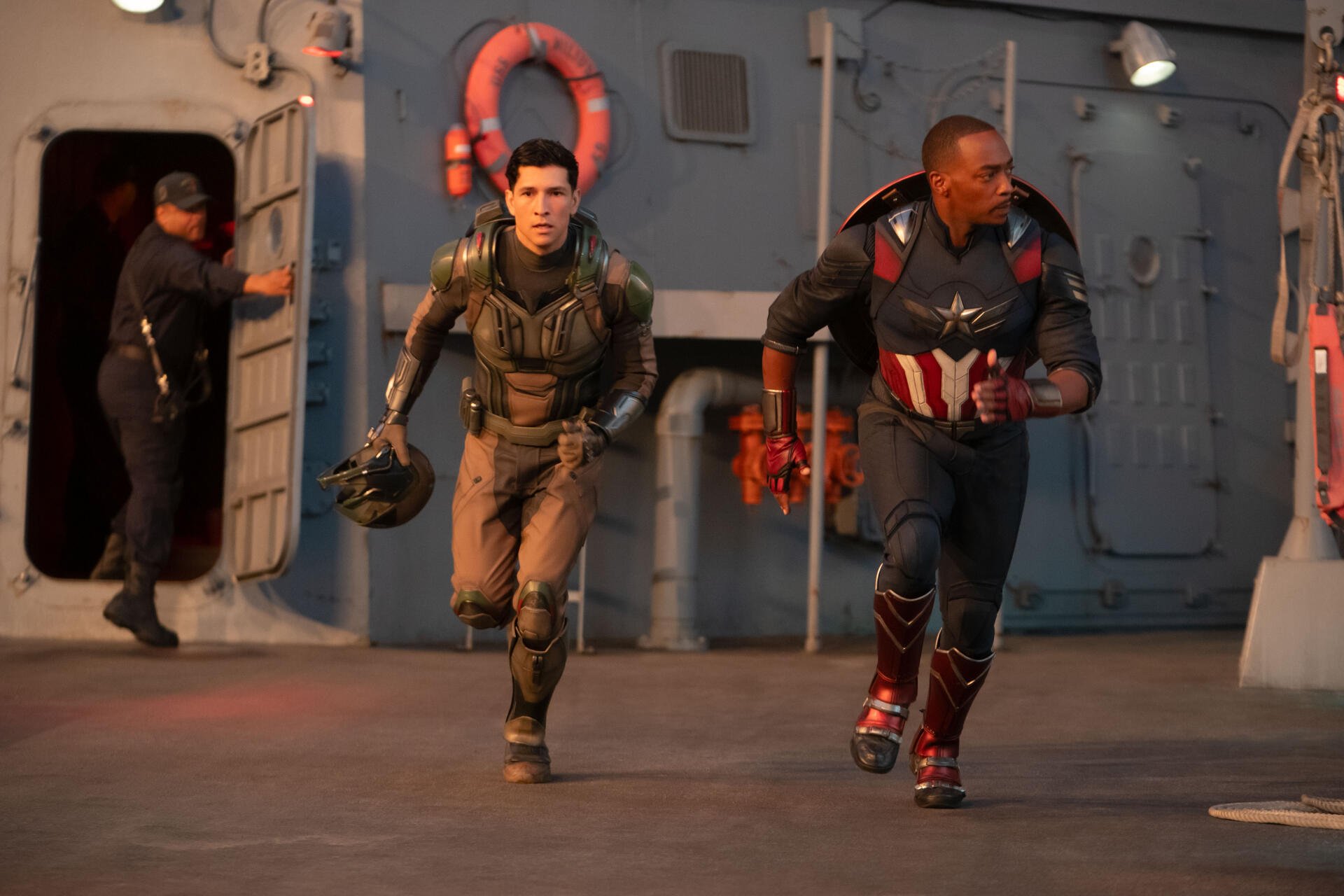 Anthony Mackie and Danny Ramirez run together in a scene from Captain America: Brave New World. The dynamic image showcases their characters in action against a vibrant backdrop.