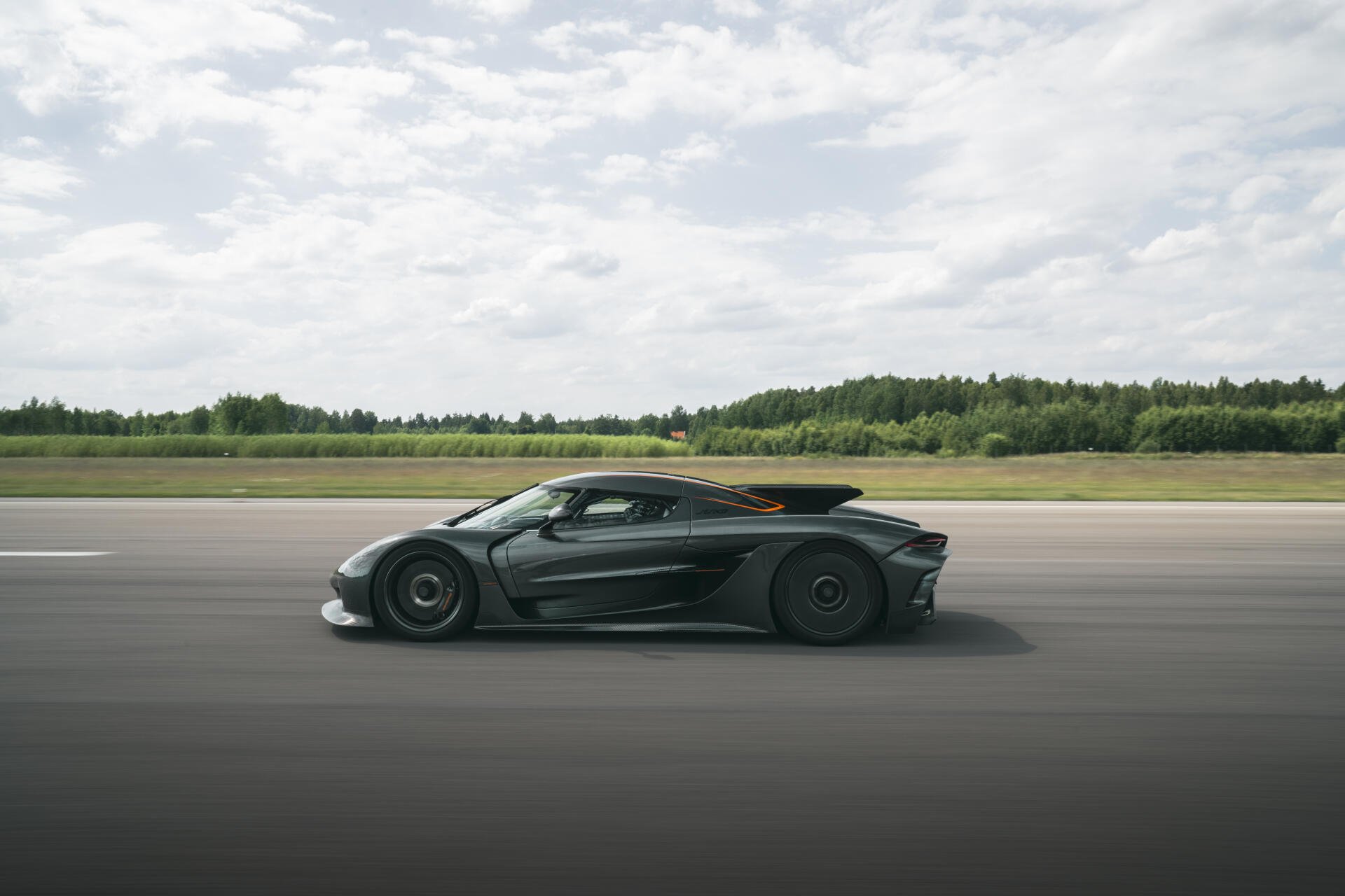 A sleek Koenigsegg Jesko Absolut speeds along an open track, showcasing its aerodynamic design against a backdrop of green fields and a cloudy sky in stunning 8K Ultra HD.