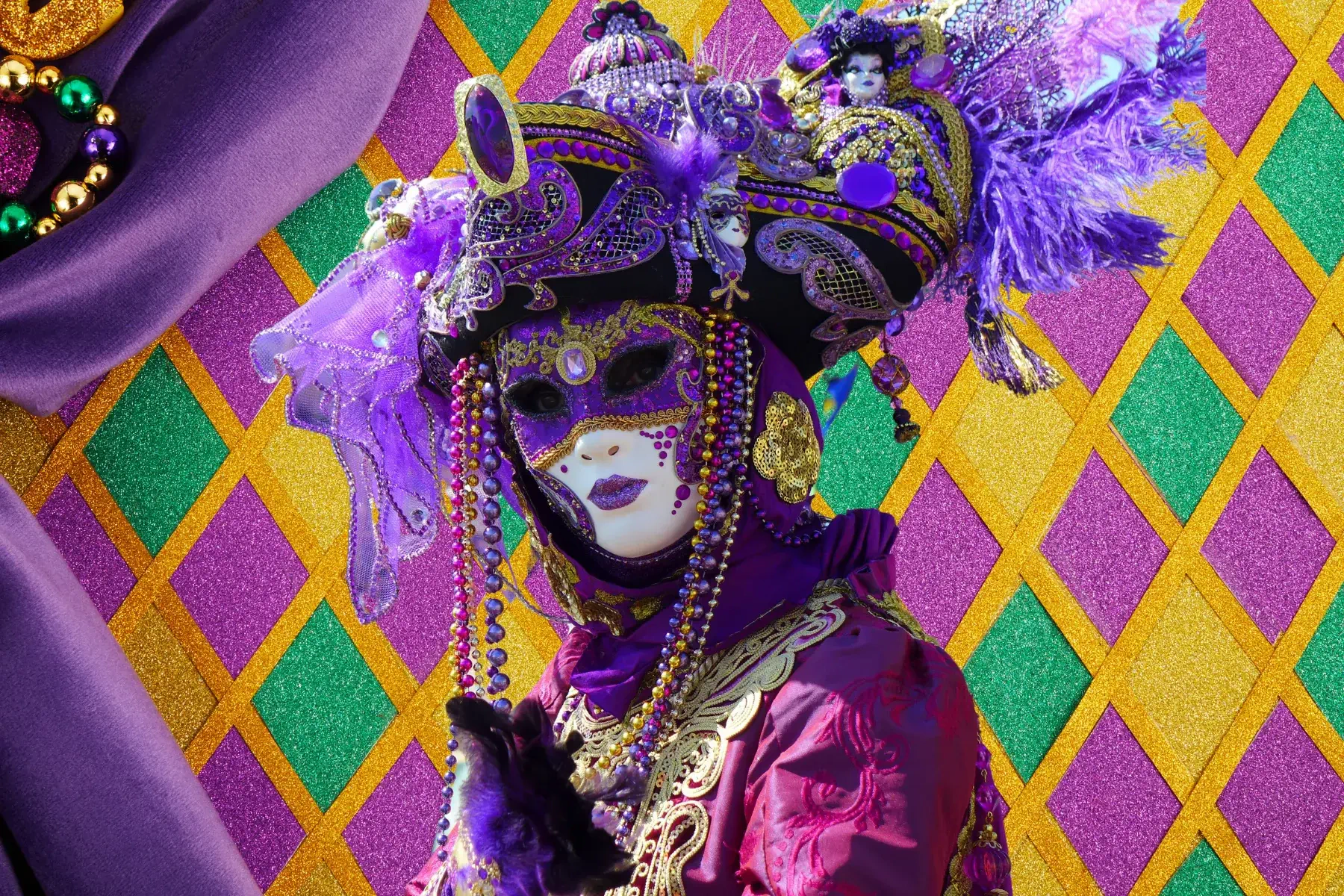 A vibrant Mardi Gras festival scene featuring a masked individual adorned in elaborate purple and gold attire, set against a colorful diamond-patterned background.