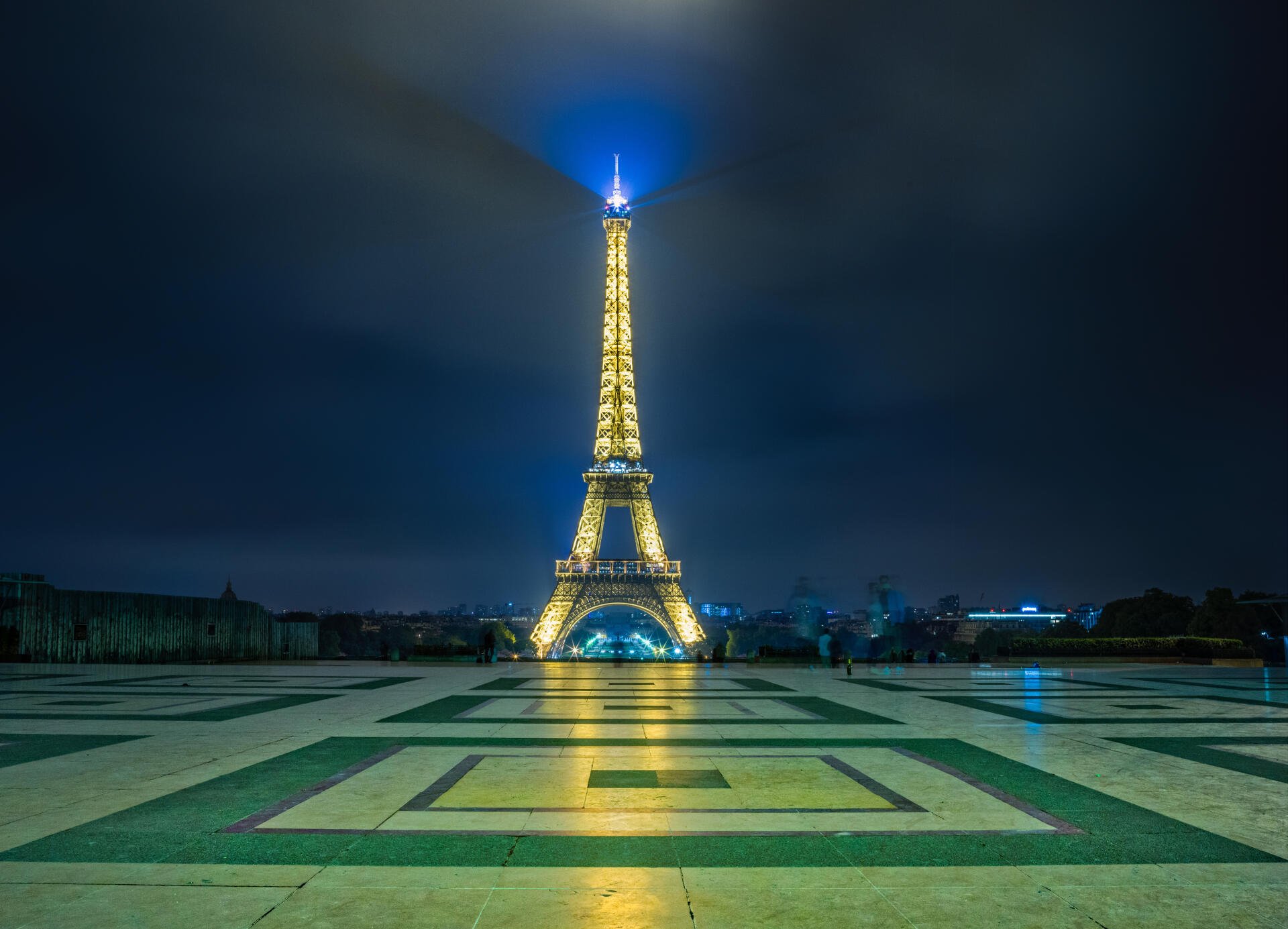 4K Ultra HD wallpaper featuring the illuminated Eiffel Tower in Paris, France, against a dark night sky with reflective pavement in the foreground.