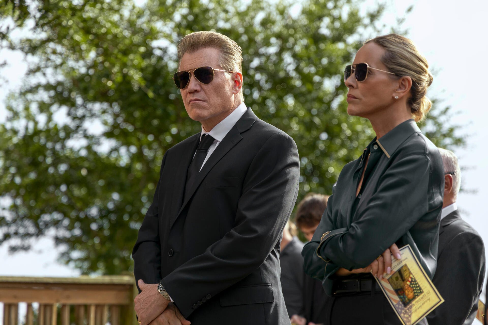 HD desktop wallpaper from the TV show The Waterfront featuring two serious characters in sunglasses standing outdoors with greenery in the background.