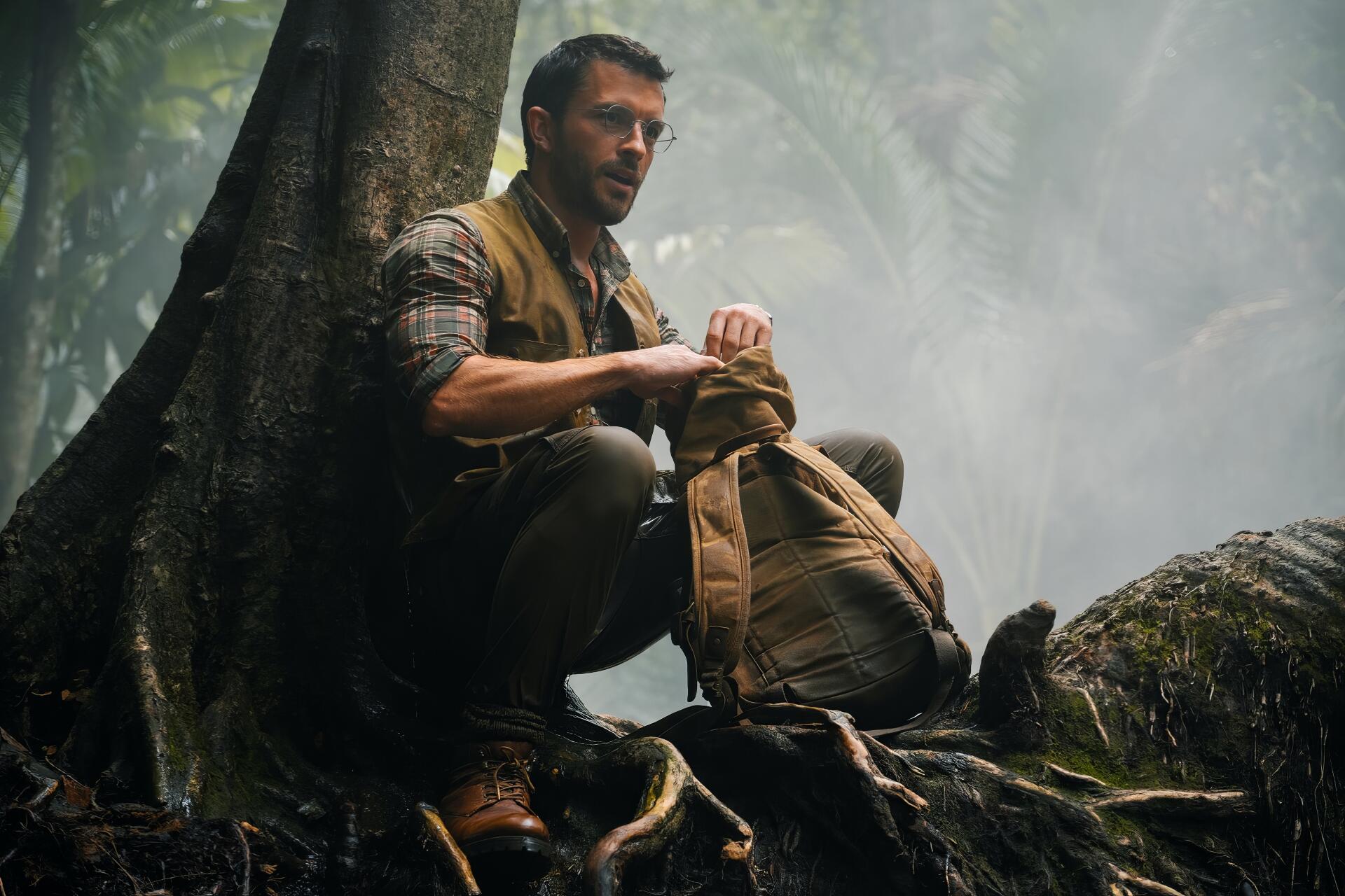 HD PC desktop wallpaper featuring Jonathan Bailey in a scene from the movie Jurassic World Rebirth, set in a misty, dense jungle environment.