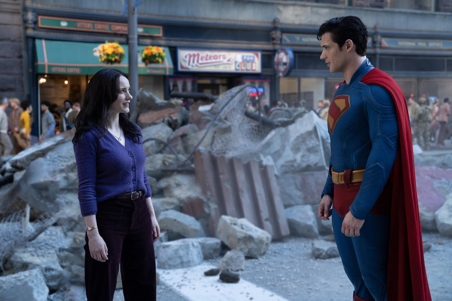 Superman (2025) in detailed 8K Ultra HD PC desktop wallpaper shows him standing in a city rubble scene, facing a woman with a tense yet calm atmosphere.