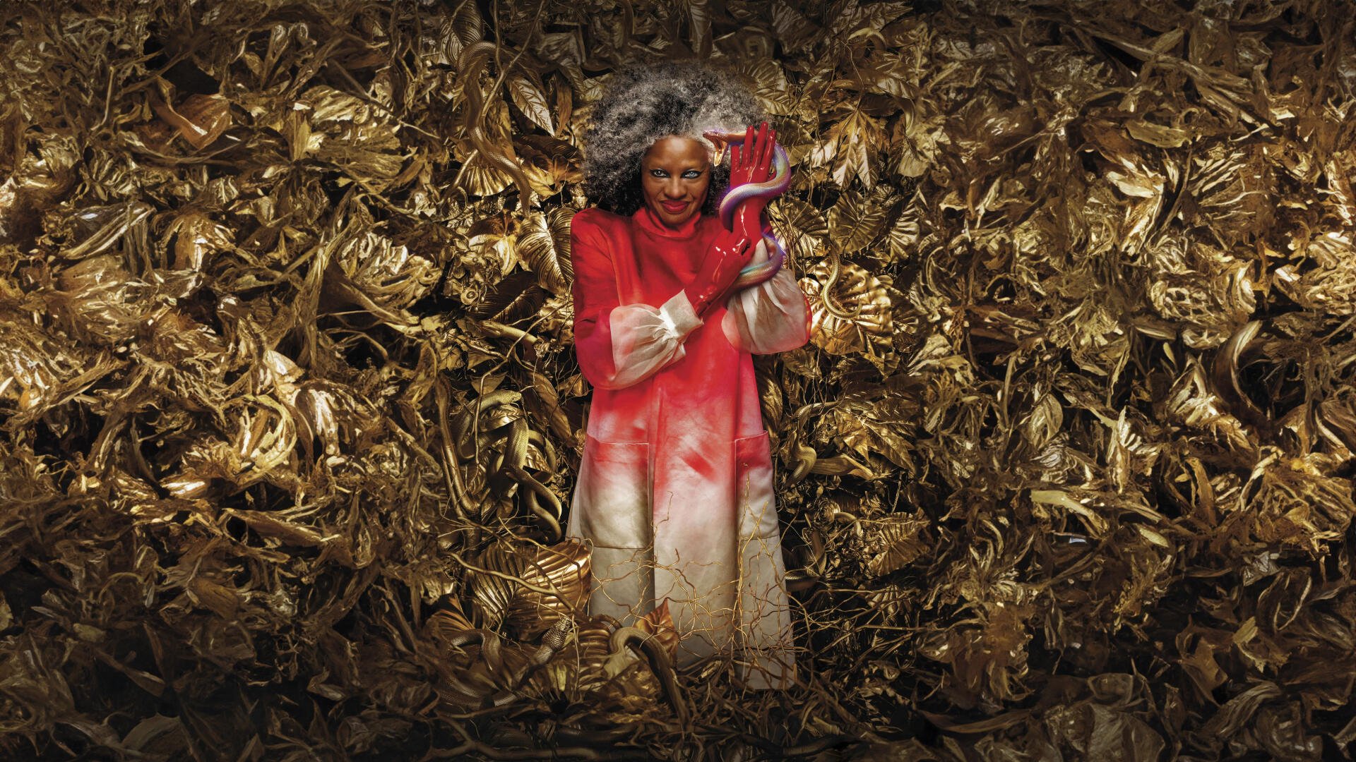 The Hunger Games: The Ballad of Songbirds & Snakes 8K Ultra HD PC Desktop Wallpaper and Background — a person in a red coat holds a red snake amid tangled golden songbird foliage.