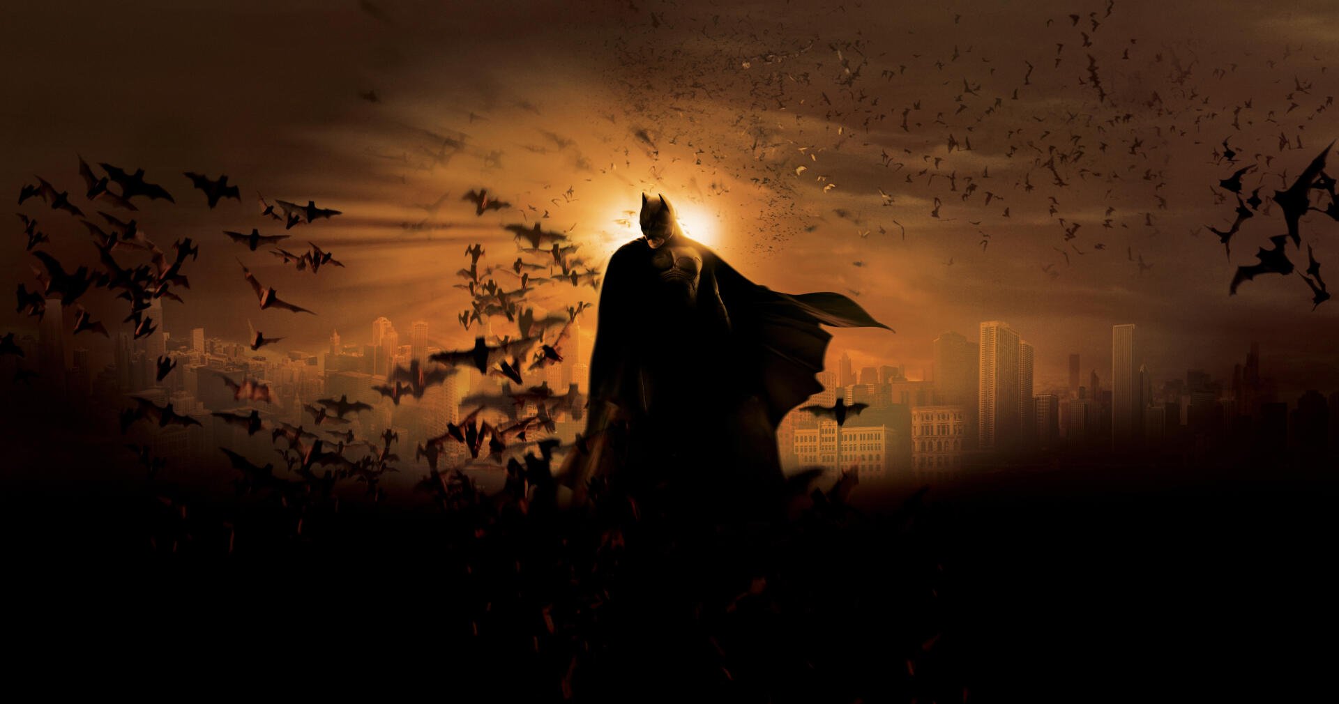 Batman Begins 4K Ultra HD PC Desktop Wallpaper and Background - silhouetted Batman stands amid a swirl of bats against a fiery orange city skyline.
