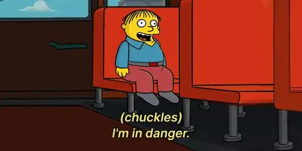 Ralph Wiggum from The Simpsons sits on a bus seat, chuckling and saying, (chuckles) I'm in danger. This image serves as a playful meme in the show's context.
