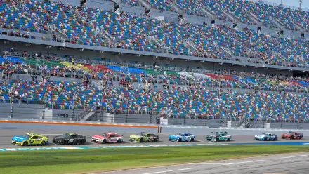 A dynamic scene from Daytona USA featuring multiple race cars speeding around the track, with colorful stands filled with enthusiastic fans in the background. HD PC desktop wallpaper.