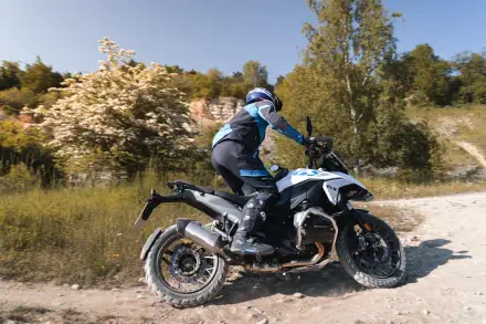 A rider maneuvers the BMW R1300GS motorcycle on a dirt path surrounded by greenery, showcasing adventure and outdoor exploration in stunning 4K Ultra HD quality.