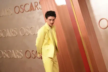 Timothée Chalamet poses in a striking yellow suit on the Oscars red carpet, against a backdrop featuring the iconic Oscars lettering. 4K Ultra HD Desktop Wallpaper.