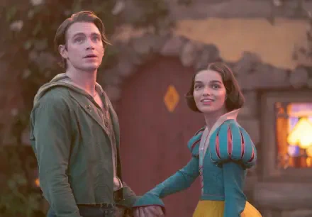 A vibrant scene from the movie Snow White (2025) featuring Andrew Burnap and Rachel Zegler. The duo gazes upward, dressed in enchanting costumes, set against a whimsical background.
