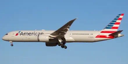 A high-resolution image of an American Airlines airplane in flight against a clear blue sky, showcasing its sleek design and vibrant tail colors.