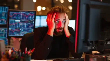 A shocked man stares at a computer screen displaying stock market data, reflecting the turmoil of a market crash. This high-resolution image captures his intense reaction.