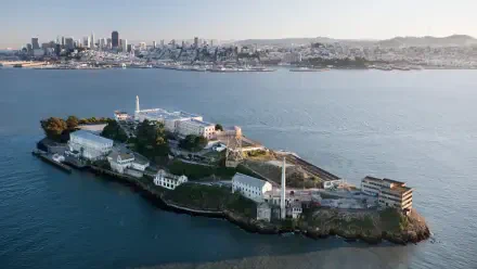 Aerial view of Alcatraz Island surrounded by water with the California coastline and city skyline in the background, captured in HD for desktop wallpaper.