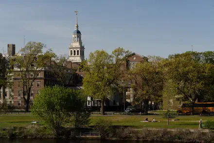 HD desktop wallpaper showing Harvard University buildings in Cambridge framed by lush green trees under a clear blue sky, blending cityscape and nature.