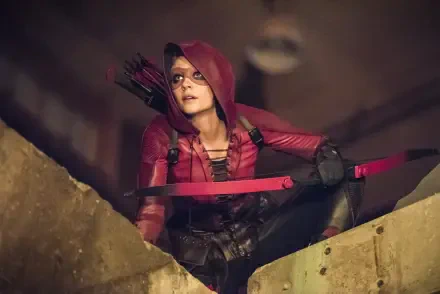 HD PC desktop wallpaper featuring a character from Arrow TV show in a red hooded outfit holding a bow and arrow, poised on a rooftop at night.