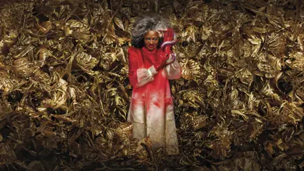 The Hunger Games: The Ballad of Songbirds & Snakes 8K Ultra HD PC Desktop Wallpaper and Background — a person in a red coat holds a red snake amid tangled golden songbird foliage.