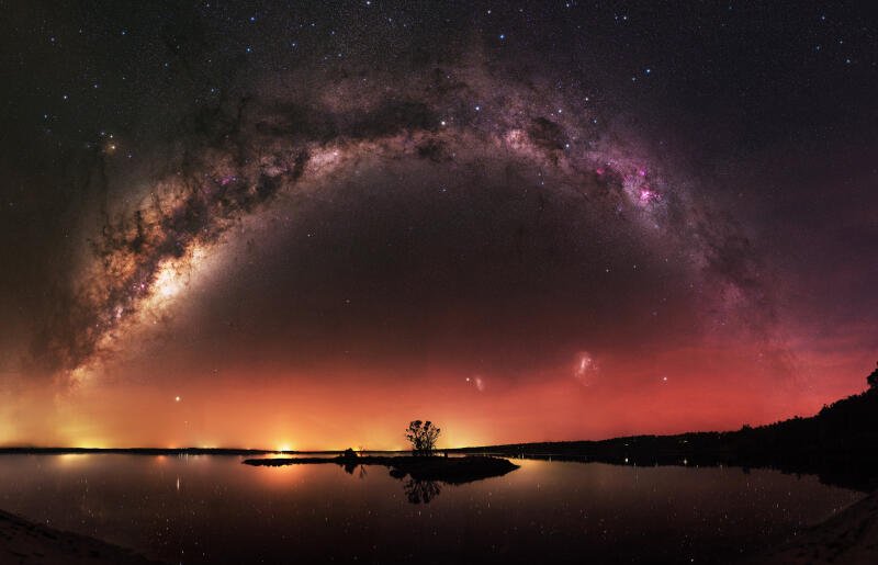 {{ A breathtaking 4K Ultra HD landscape featuring the Milky Way arching over a calm lake with nebula colors reflecting on the water, creating a stunning galaxy scene.