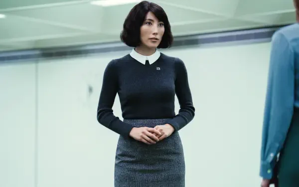 A still from the TV show Severance, featuring Dichen Lachman. The image showcases her poised in a modern, minimalist setting, emphasizing her stylish attire.