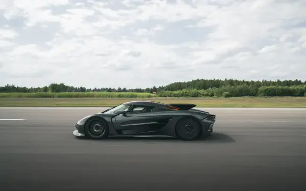A sleek Koenigsegg Jesko Absolut speeds along an open track, showcasing its aerodynamic design against a backdrop of green fields and a cloudy sky in stunning 8K Ultra HD.