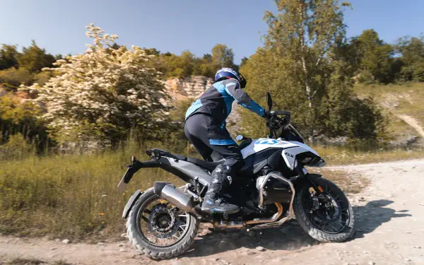 A rider maneuvers the BMW R1300GS motorcycle on a dirt path surrounded by greenery, showcasing adventure and outdoor exploration in stunning 4K Ultra HD quality.