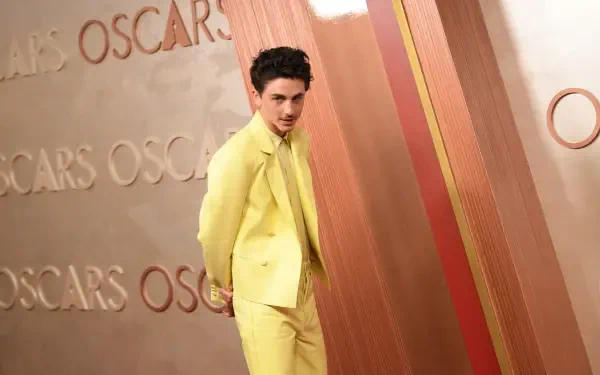 Timothée Chalamet poses in a striking yellow suit on the Oscars red carpet, against a backdrop featuring the iconic Oscars lettering. 4K Ultra HD Desktop Wallpaper.