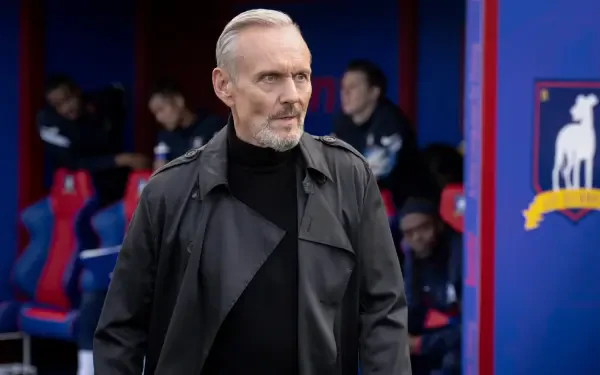 Anthony Head appears in a scene from the TV show Ted Lasso, featuring a dramatic close-up in a sports locker room, set against a vibrant team backdrop. 4K Ultra HD quality adds depth.