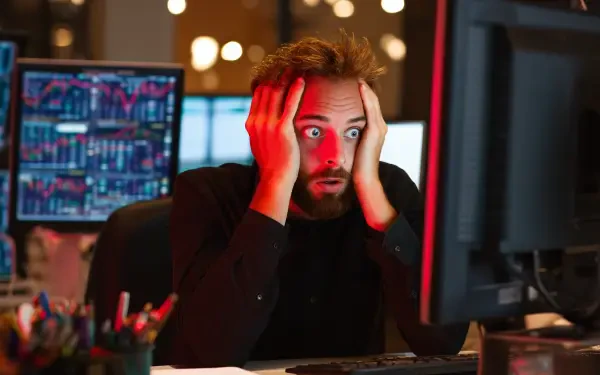 A shocked man stares at a computer screen displaying stock market data, reflecting the turmoil of a market crash. This high-resolution image captures his intense reaction.