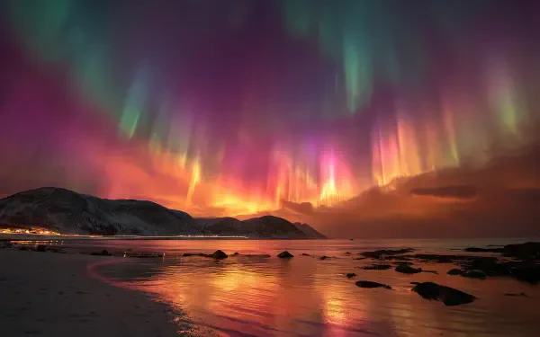 HD desktop wallpaper of vibrant Northern Lights dancing over a calm ocean beach with silhouetted hills under a colorful night sky.