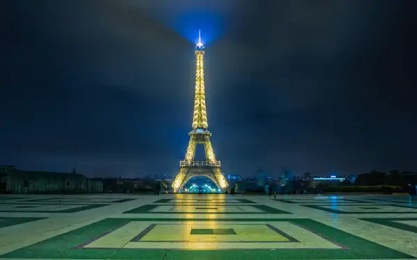 4K Ultra HD wallpaper featuring the illuminated Eiffel Tower in Paris, France, against a dark night sky with reflective pavement in the foreground.