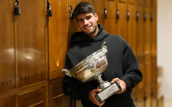 Carlos Alcaraz poses with a large trophy inside a wooden locker room, celebrating his victory at The French Open (Roland Garros) in this HD tennis-themed desktop wallpaper.