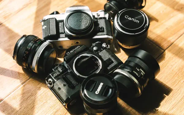 Vintage Canon cameras and lenses arranged on a wooden surface, captured in sharp 4K Ultra HD quality for a striking man-made PC desktop wallpaper.