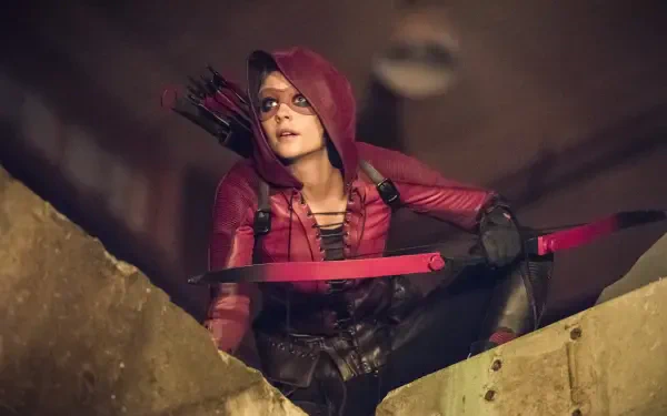 HD PC desktop wallpaper featuring a character from Arrow TV show in a red hooded outfit holding a bow and arrow, poised on a rooftop at night.