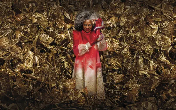 The Hunger Games: The Ballad of Songbirds & Snakes 8K Ultra HD PC Desktop Wallpaper and Background — a person in a red coat holds a red snake amid tangled golden songbird foliage.