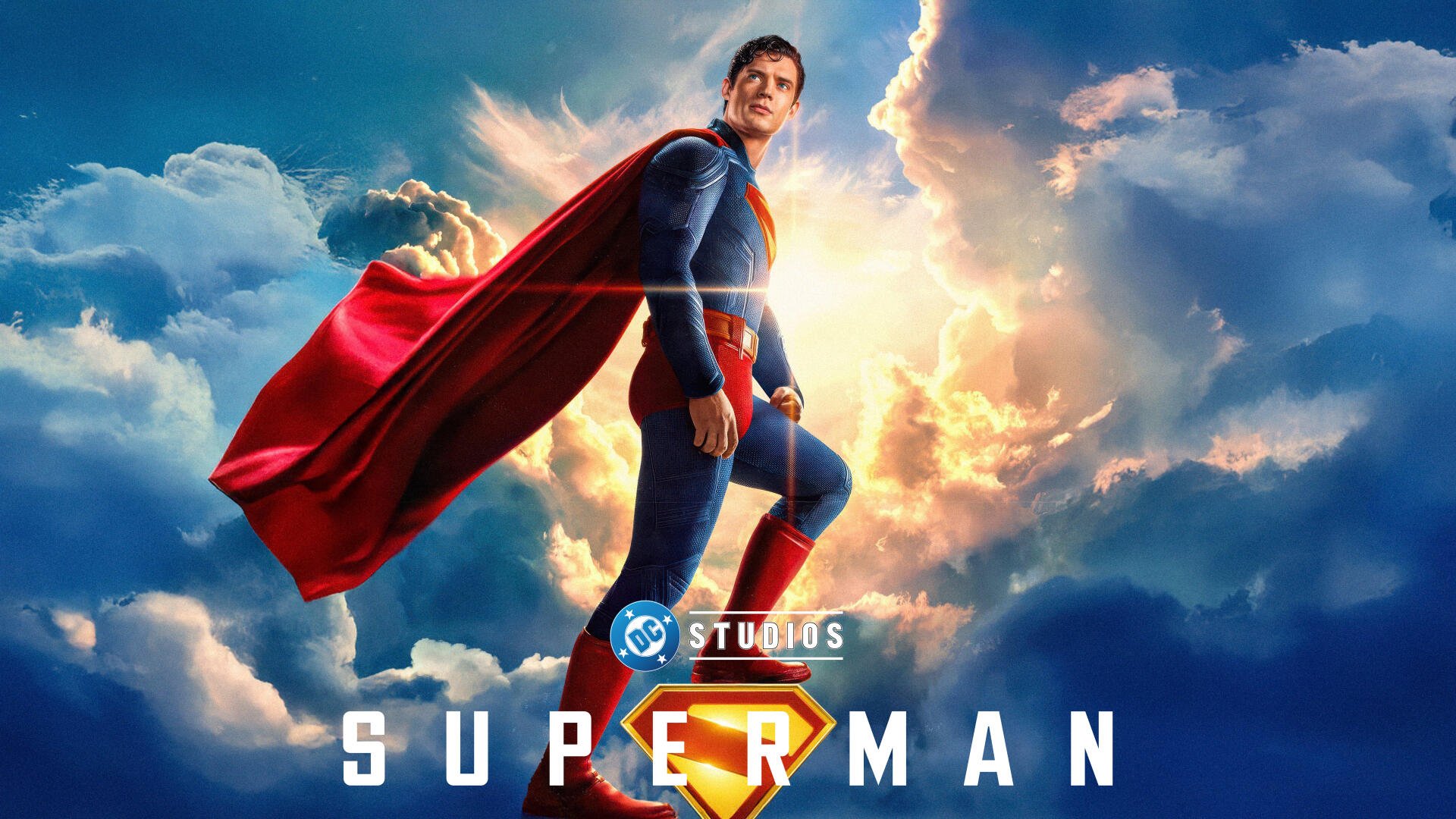 Superman (2025) 4K Ultra HD PC desktop wallpaper: Superman stands on a cloud-lit peak, red cape billowing against a dramatic sunburst sky.