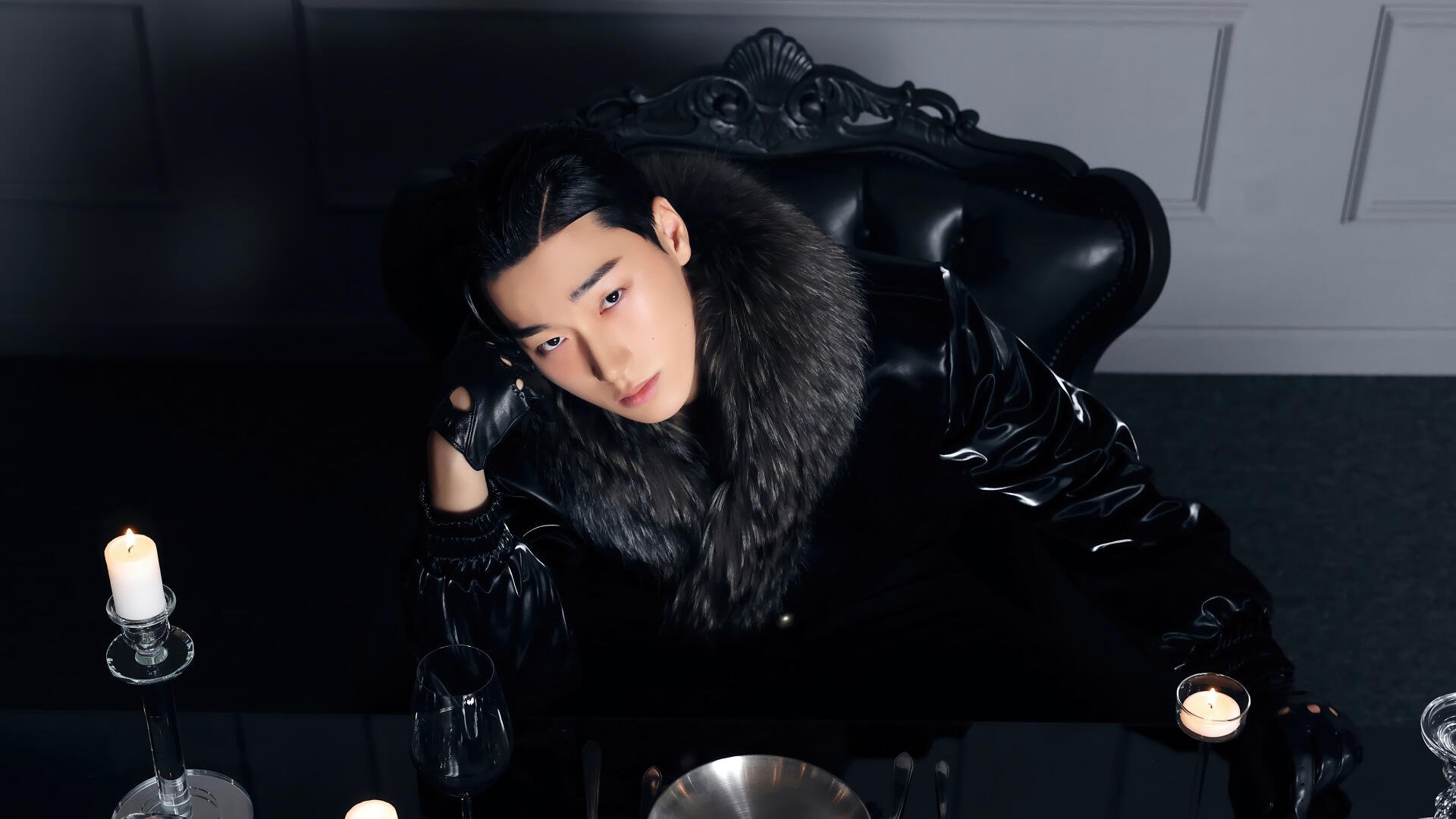 K-pop ATEEZ-inspired black 4K desktop wallpaper: solitary figure in glossy black coat with fur collar reclining at a candlelit table, moody high-contrast portrait.