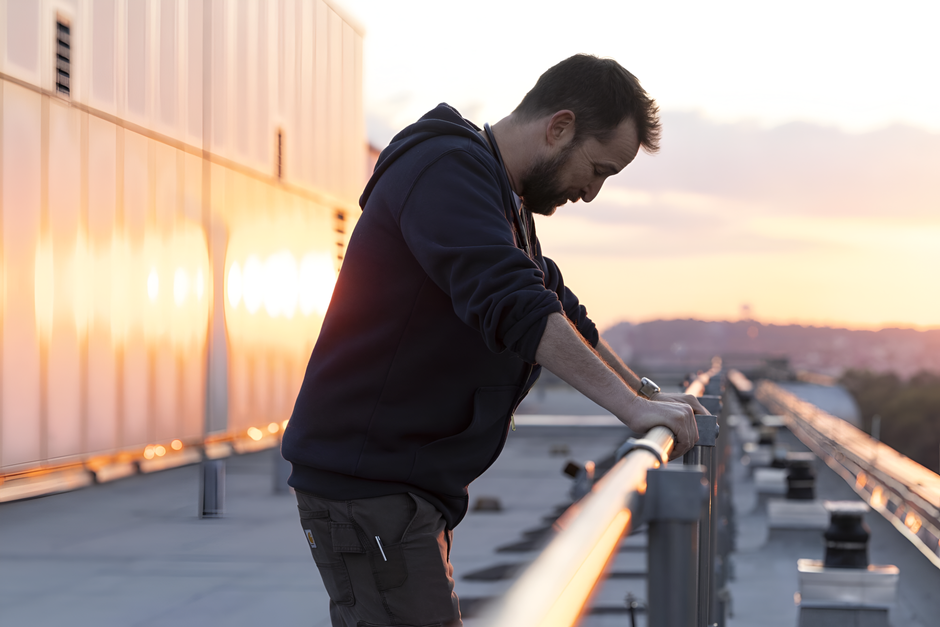 4K PC wallpaper from TV show The Pitt: solitary male actor leans on a rooftop railing at sunset, reflective and moody atmosphere.