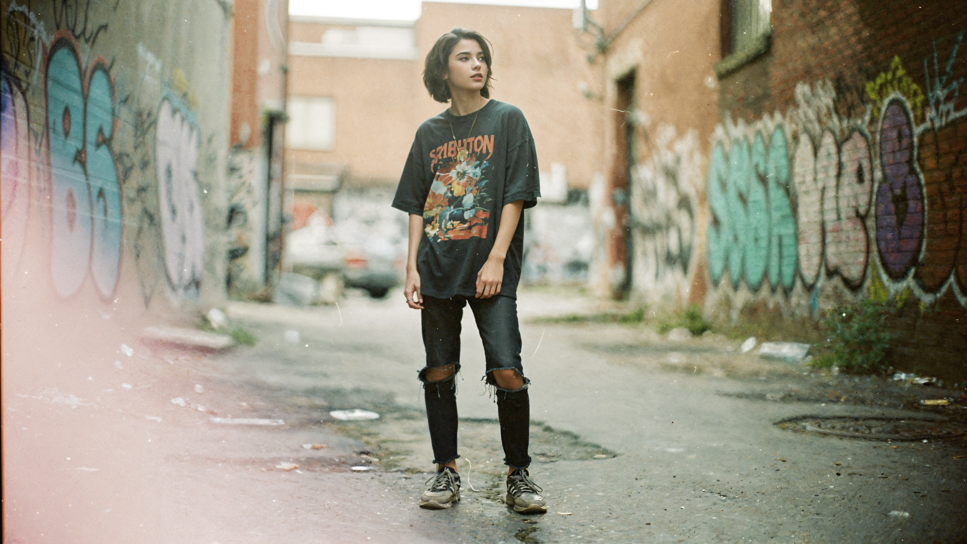 Soft grunge 4K Ultra HD PC Desktop Wallpaper and Background: solitary person in ripped jeans and a band tee stands in a graffiti-lined urban alley, muted colors and hazy film-like light.